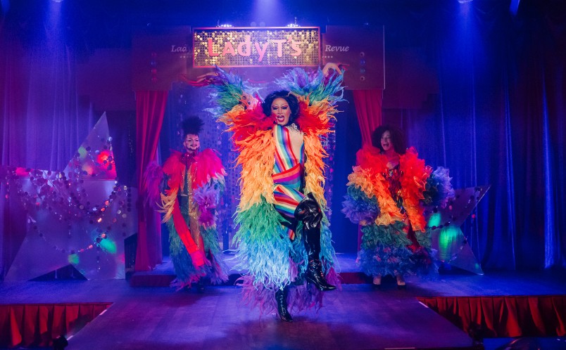 3 Drag performers dancing on the stage in rainbow coloured costumes