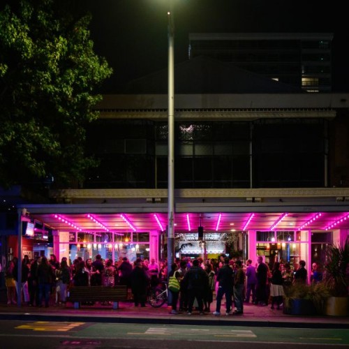 A crowd of people on the sidewalk in front of Q Theatre lit up at night