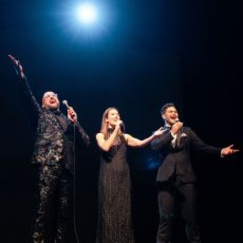 Performers Luke, Shaan & Kawiti onstage singing with a bright light breaking through them 