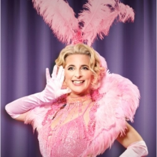 Comedian Felicity Ward dressed in a pink old hollywood dress and feather hat, throwing jazz hands and gleaming with enthusiasm
