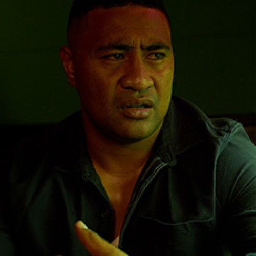 Actor Beulah Koale looking off to the side, with dark shadows and a dark green background