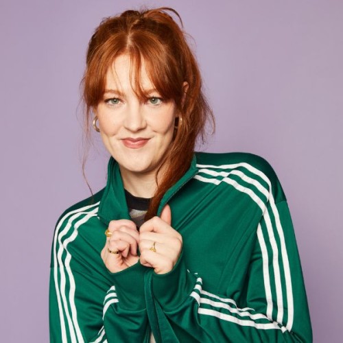 An image of Lou Wall red hair tied in a pony, popping the collar of a green adidas tracksuit
