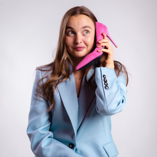 n image of Emma in a blue suit answering a pink heel as if it's a mobile phone. 