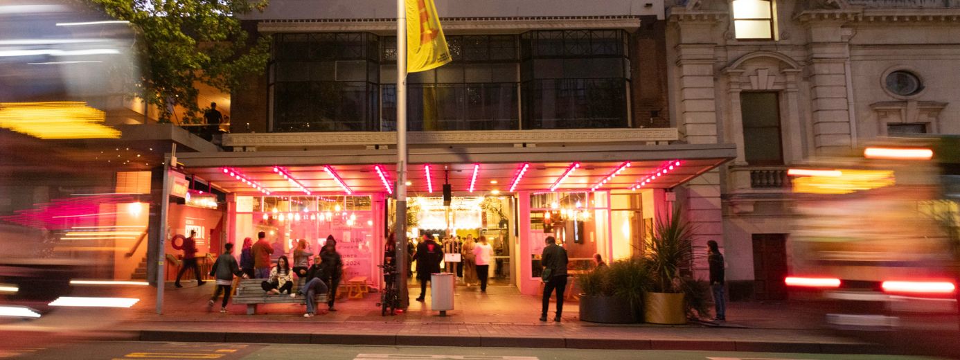 Q theatre from street scene at night, featuring a modern, well-lit venue with pink lights under a canopy. 