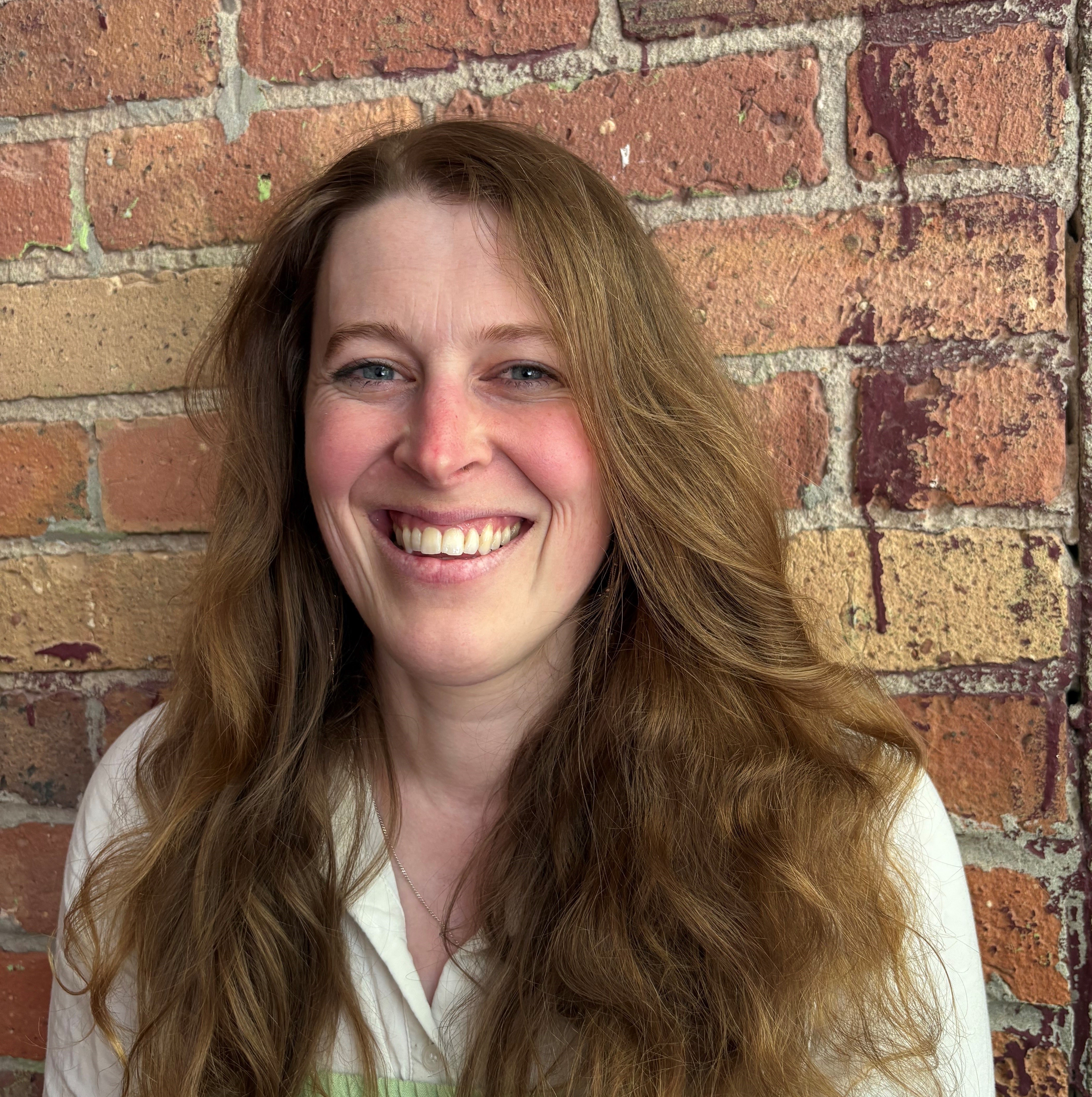 A photo of Alice smiling in front of a brick wall 