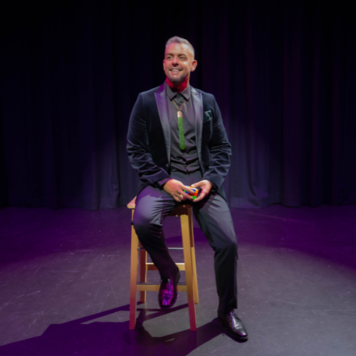 An image of Steven Taputoro sitting on a stool agaisnt  a black background